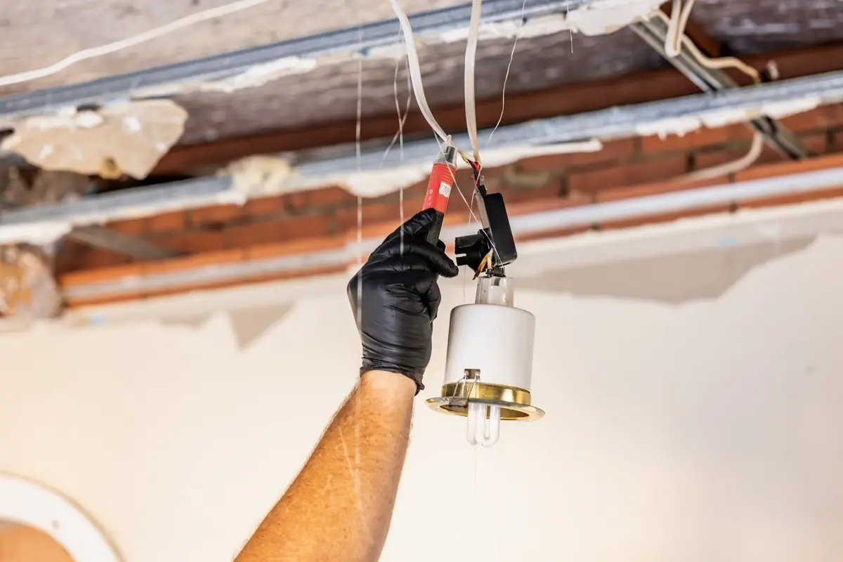 Inspector checking a light fitting beneath an exposed ceiling for a building defect report