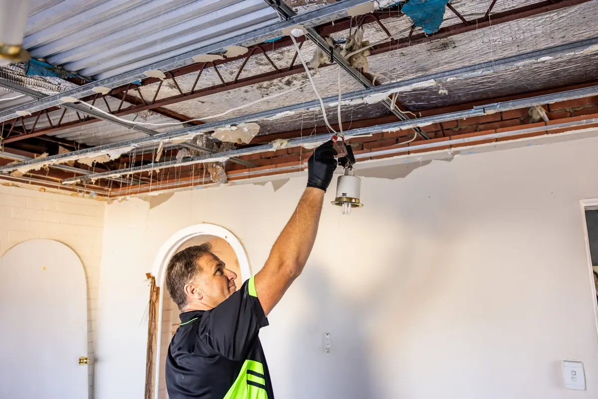 Inspector checking a light fitting below exposed ceiling framing during an owner-builder inspection