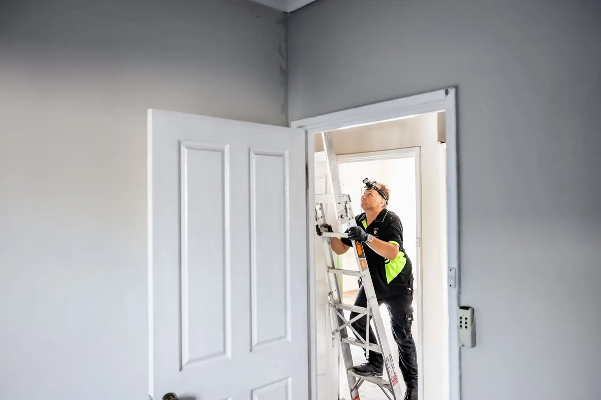 Building inspector on a ladder checking the ceiling area during a strata inspection in Perth