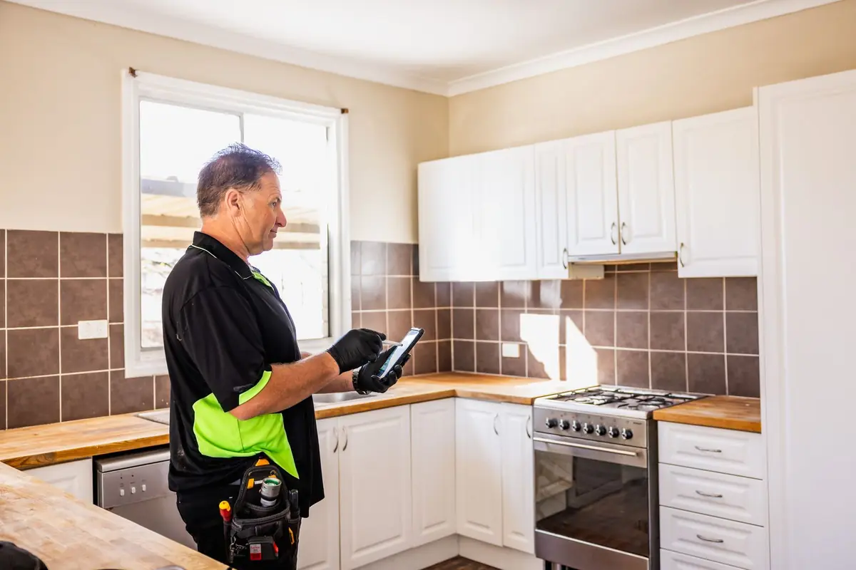 Inspector recording kitchen condition on a phone during a strata inspection in Perth